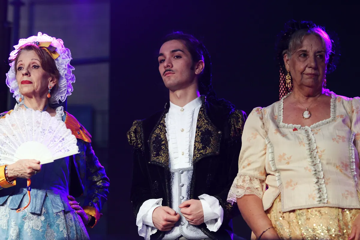 A woman in a black lace headdress and a young man in a dark embroidered jacket in costume on a stage.