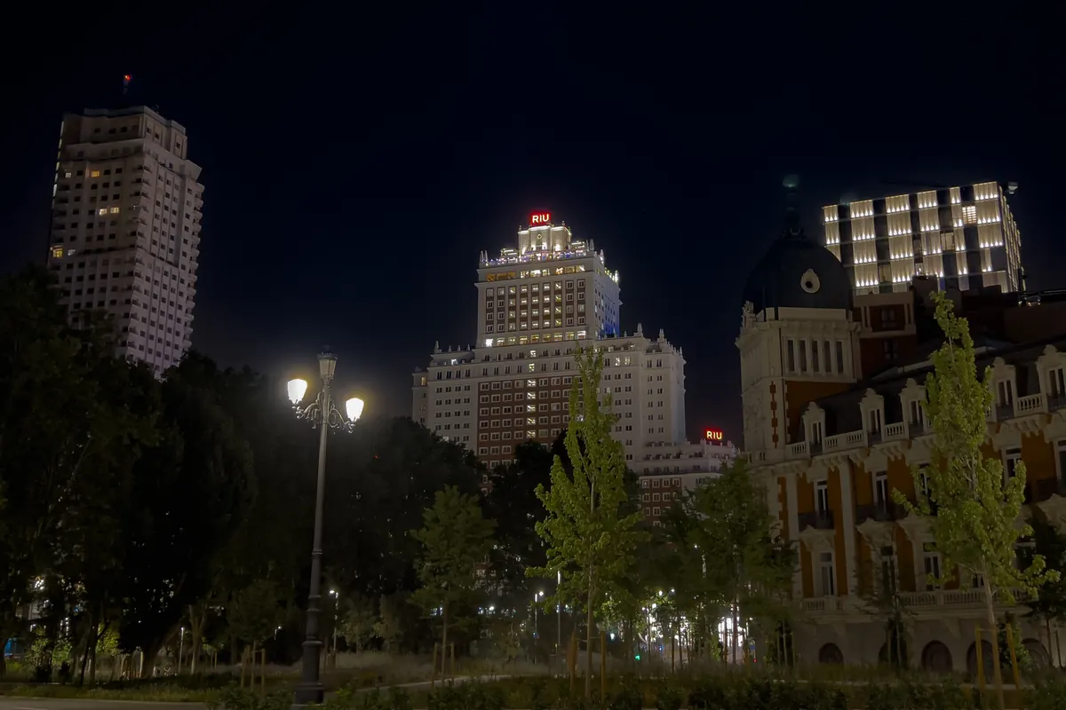 Lit buildings, trees and a street lamp in Plaza de España at night.
